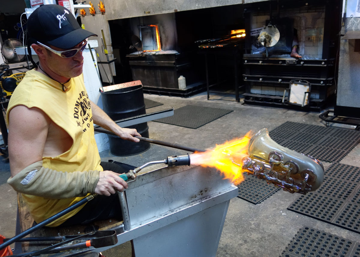 alt="Master glassblower Robert Stern torches the blowpipe"