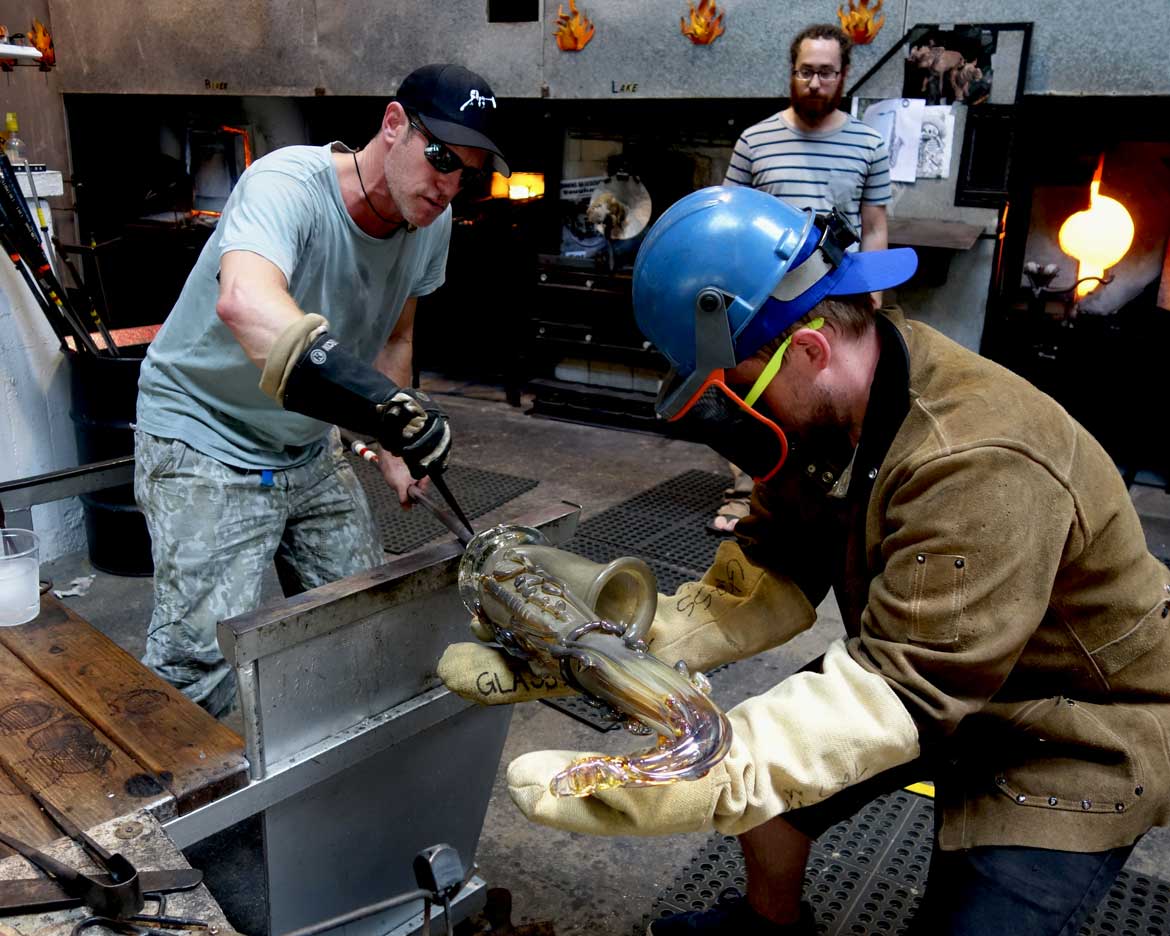 alt="Resident glassblower Kyle Herr helps Robert Stern in initiating the crack-off"